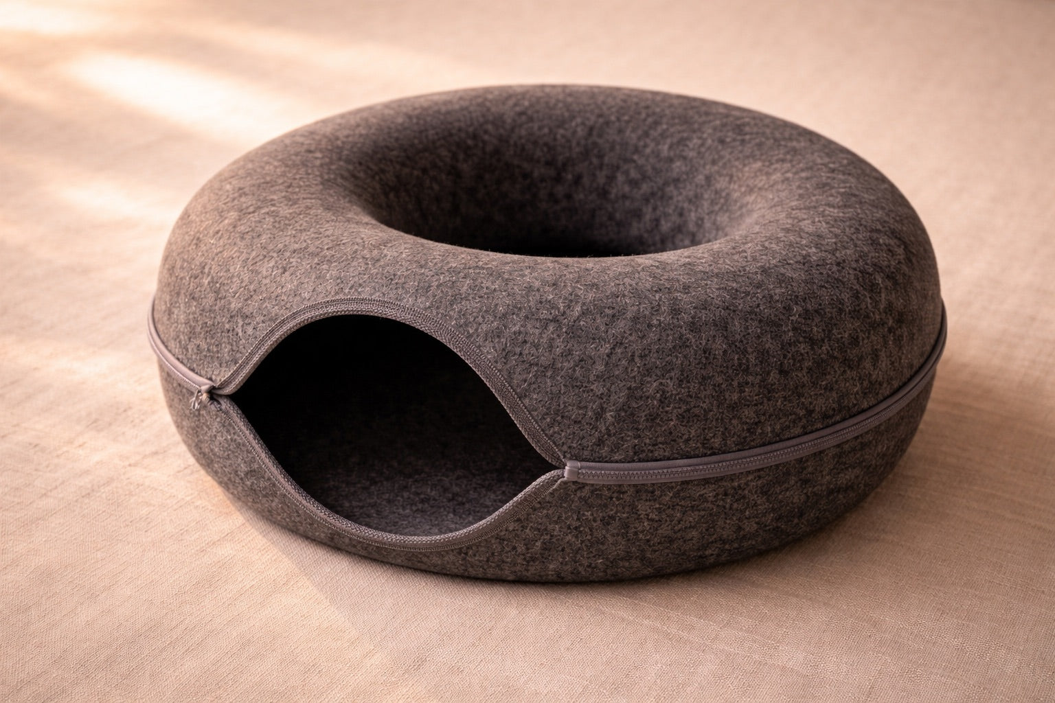 Charcoal wool felt cat tunnel bed on a cream linen surface, showing material texture and quality
